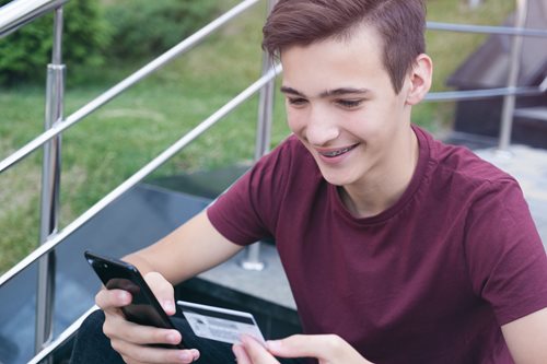 happy teenage boy looking at phone and debit card